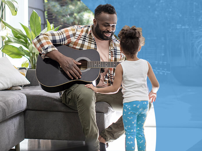 A father playing guitar for his young daughter at home